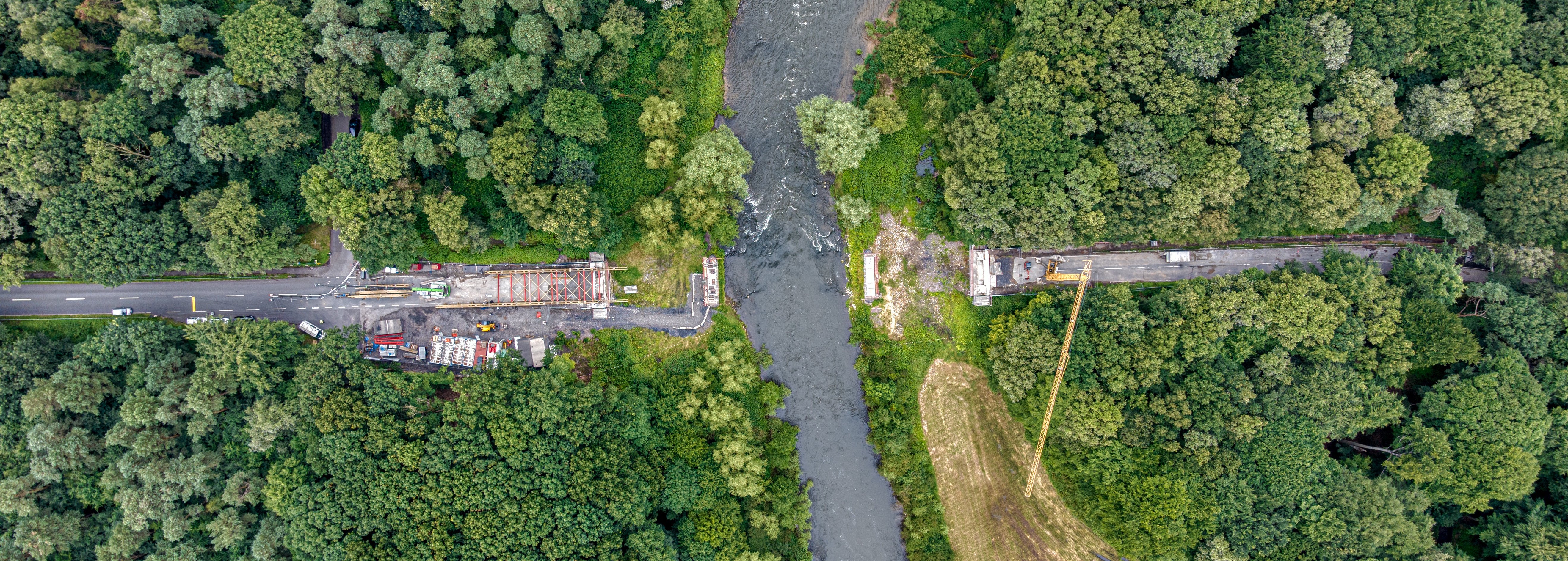Brückensystem im Bau aus der Vogelperspektive über einem Fluss, umgeben von Wald
