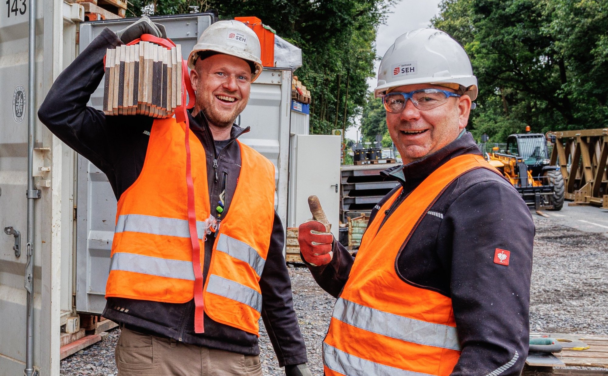 Zwei lächelnde Mitarbeiter mit Schutzkleidung und Helm