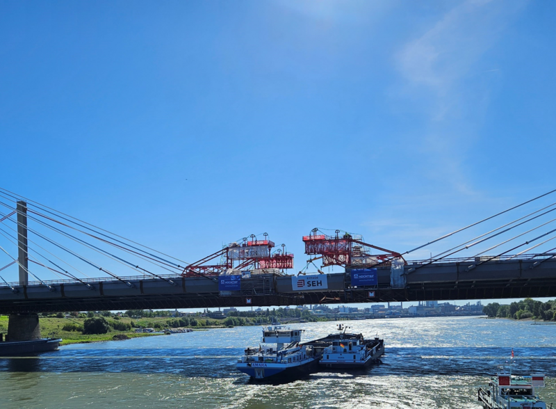 Lückenschluss der Brücke bei strahlendem Wetter. Schiff fährt unter der Brücke hindurch. 