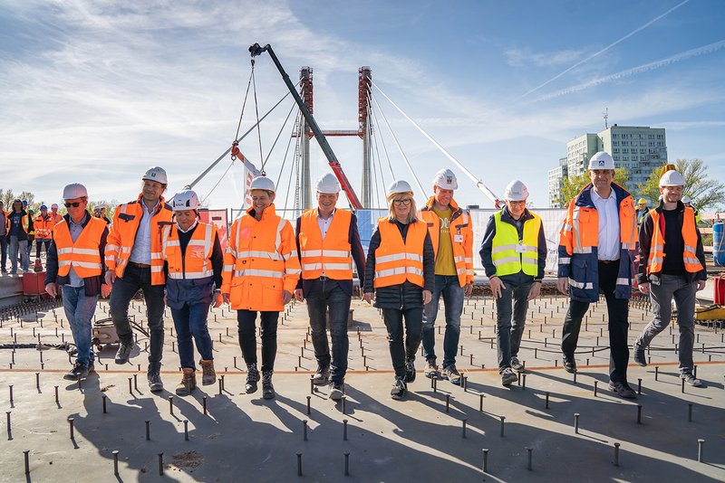 Gruppenbild Projektbeteiligter mit Helm und Warnweste. Gehen über die Brücke.