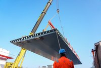 Mitarbeiter beobachtet großes Bauteil, welches mit einem Kran angehoben wurde.