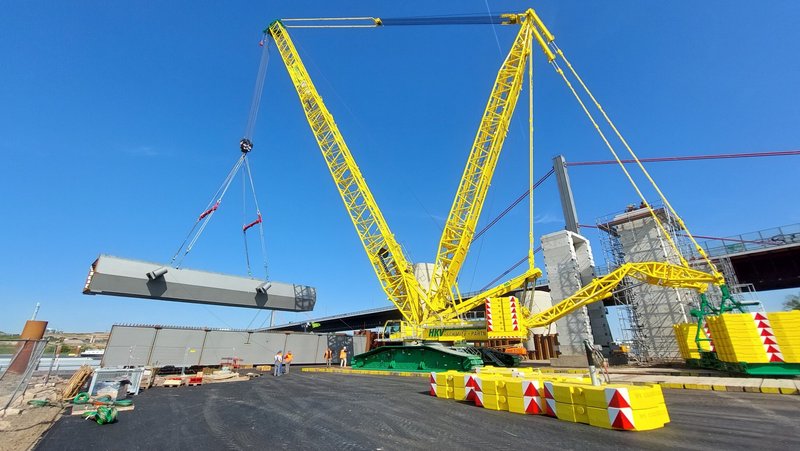 Ein großer gelber Kran hebt ein Bauteil.